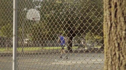 Young man shooting hoops at an outdoor basketball court. Slider shot. Stock Footage 80342880