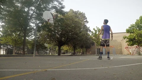 Young man shooting hoops at an outdoor basketball court. Stock Footage 80344932