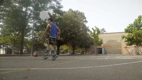 Young man shooting hoops at an outdoor basketball court. Stock Footage 80346237