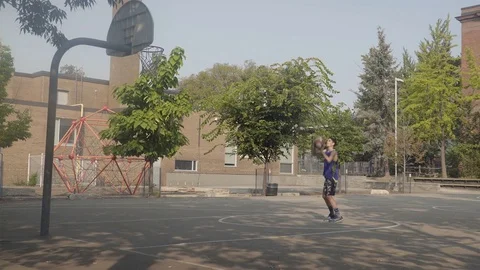 Young man shooting hoops at an outdoor basketball court. Stock Footage 80347576