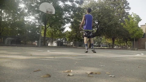 Young man shooting hoops at an outdoor basketball court. Stock Footage 80351606