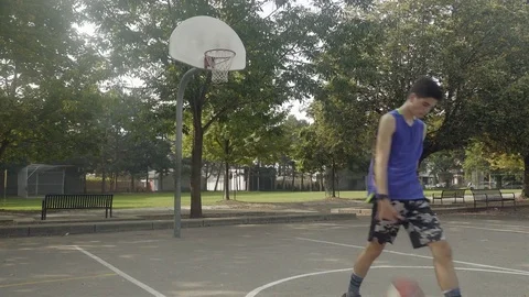 Young man shooting hoops at an outdoor basketball court. Stock Footage 80354512