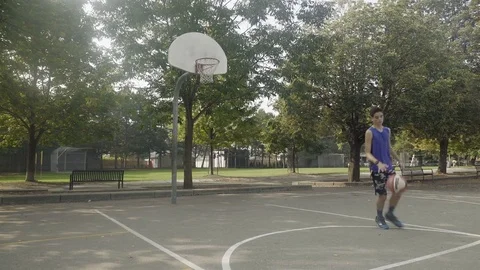 Young man shooting hoops at an outdoor basketball court. Stock Footage 80354751