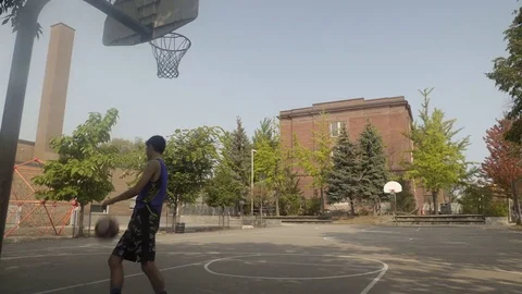Young man shooting hoops at an outdoor basketball court. Stock Footage 80356484
