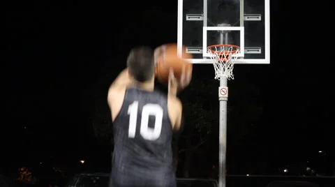 A young man shooting three-pointers on an outdoor basketball court at night. Stock Footage 67984816