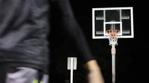 A young man shooting three-pointers on an outdoor basketball court at night. Stock Footage 67984869