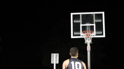 A young man shooting three-pointers on an outdoor basketball court at night. Stock Footage 67984876