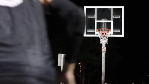 A young man shooting three-pointers on an outdoor basketball court at night. Stock Footage 71092555