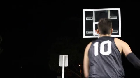 A young man shooting three-pointers on an outdoor basketball court at night. Stock Footage 71092583