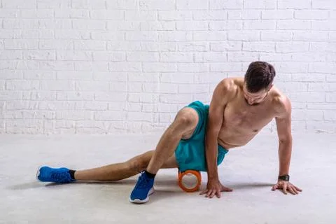 A young man in shorts does exercises on a roller from foam to his legs. Stock Photos