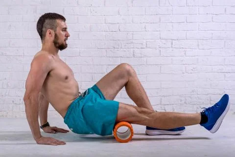 A young man in shorts does exercises on a roller from foam to his legs. Foto stock