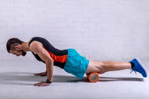 A young man in shorts does exercises on a roller from foam to his legs. Foto stock