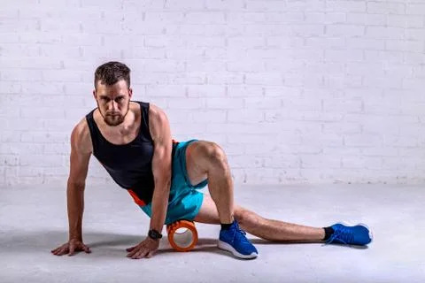 A young man in shorts does exercises on a roller from foam to his legs. Stock Photos