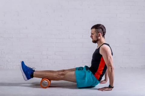 A young man in shorts does exercises on a roller from foam to his legs. Stock Photos