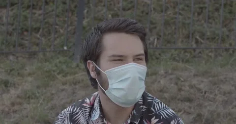Young man is shouting something via surgical mask, then cheekily looking Stock Footage 136900725