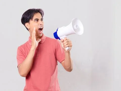 Young man shouting through a megaphone with one hand over his mouth, making.. Stock Photos