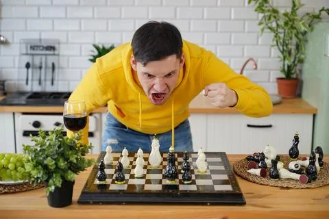 Young man shouts while playing chess on kitchen table. Emotional male plays in Stock Photos
