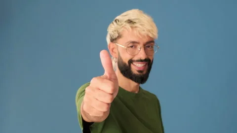 Young man showing thumb up gesture, isolated on blue background in studio Stock Footage 303288830