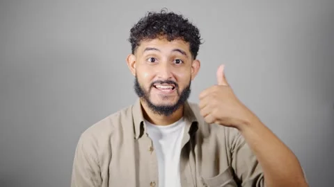 Young man showing thumbs up with different expressions on gray background Video stock 314785568