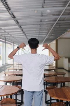 Young man showing thumbs down gesture in empty cafeteria setting Stock Photos