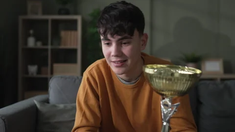 Young man showing off trophy during video call Stock Footage 328361103