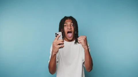 Young man shows surprise while looking at his smartphone against a blue bac.. Stock Footage 313273695