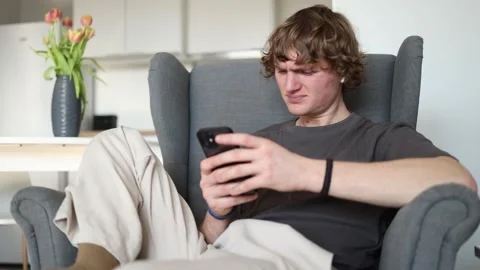 A young man shows a surprised and puzzled expression while holding a phone, as i Stock Footage 302634411