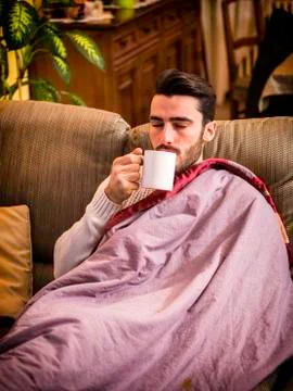 Young man sick with flu drinking herbal tea Stock Photos