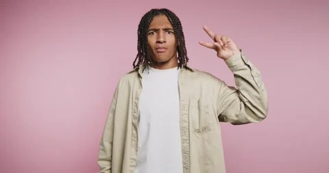 Young man signs peace symbol in front of pink background while smiling and .. Vídeo Stock 326788053
