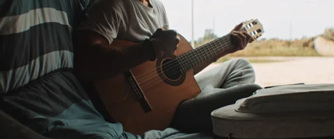 Young man singing and playing the guitar in back of campig van Stock Footage 203584206