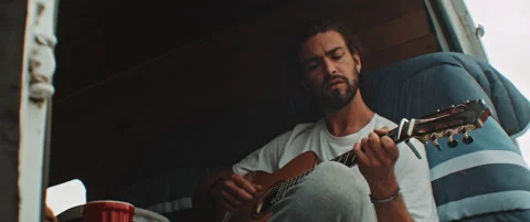 Young man singing and playing the guitar in back of campig van Stock Footage 203584208