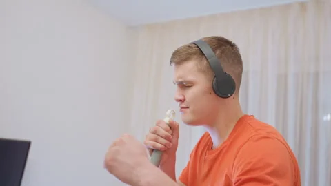 Young Man Singing With Mop Handle While Listening To Music On Headphones Stock Footage 319914786