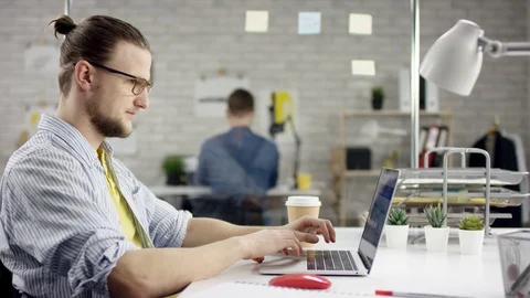 Young man singing sitting at office desk with laptop surrounded by diverse Stock Footage 105018968