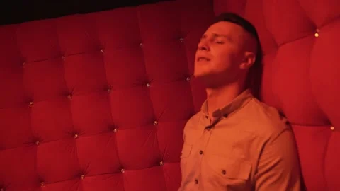 Young man singing on a sofa in red room of nightclub. Shooting music video Stock Footage 213605599