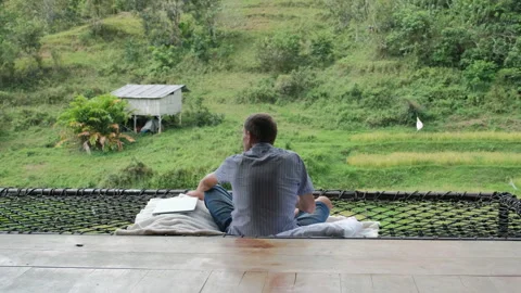 Young man sipping coffee on hammock in jungle hut Vídeo Stock 307079412
