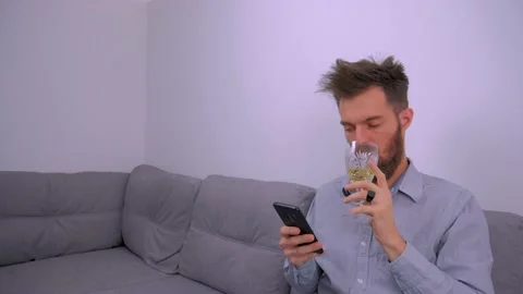 Young Man Sips an Alcoholic Drink and Scrolls Smartphone, Tracking Shot Stock Footage 133050629