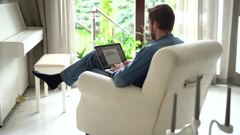 Young man sit in armchair use laptop, working distantly using wireless tech Stock Footage 155331388