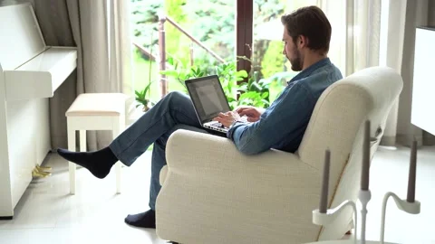 Young man sit in armchair use laptop, working distantly using wireless tech Stock Footage 155331391
