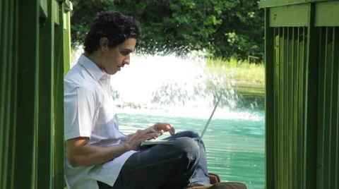 Young man sit on dock with laptop. fountain in B/G Stock Footage 45523788