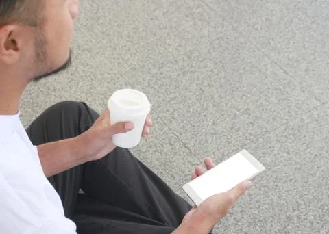 Young man sit drinking coffee from disposable take away cup and smartphone Stock Photos