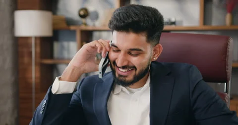 Young man sit indoor talking on smartphone in office employee holding cellphone Stock Footage 220139870
