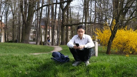 Young man sit watch use smart phone mobile in a spring park nature in Wroclaw Stock Footage 88569472