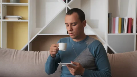Young man siting on sofa enjoying fresh new day feeling rested drinking coffee Video stock 134872514