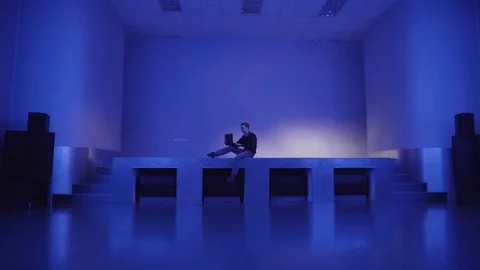 A young man sits alone on an empty dance floors and uses laptop to invite 库存影片 71492574