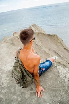 Young man sits alone looking out to sea / Man relaxing on beach, ocean view Foto stock