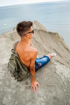 Young man sits alone looking out to sea / Man relaxing on beach, ocean view / Foto stock