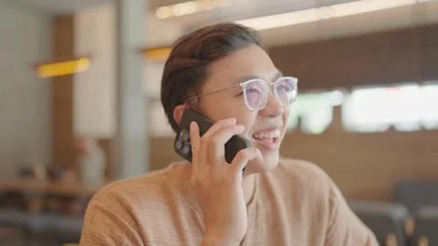 A young man sits and talks on the phone in a coffee shop. Stock Footage 251974215