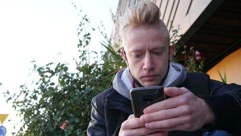 Young Man sits and use Mobile Smart Phone on a Street Stock Footage 142764985
