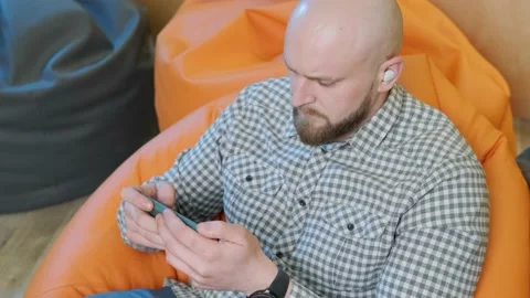 Young man sits on a bean bag while playing online using his phone. Stock Footage 152727643