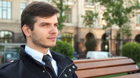 A young man sits on a bench and drinks coffee Stock Footage 83175541